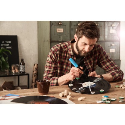 Muž lepí dekorace na vinylovou desku pomocí modré tavné lepicí pistole Bosch Gluey. Tavná pistole pro řemeslné projekty. Muž lepí dekorace na vinylovou desku pomocí modré tavné lepicí pistole Bosch Gluey. Tavná pistole pro řemeslné projekty.