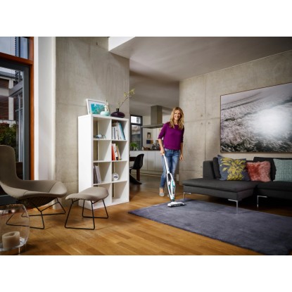 Žena vysává koberec pomocí akumulátorového vysavače Leifheit Regulus PowerVac. Akumulátorový ruční vysavač. Žena vysává koberec pomocí akumulátorového vysavače Leifheit Regulus PowerVac. Akumulátorový ruční vysavač.