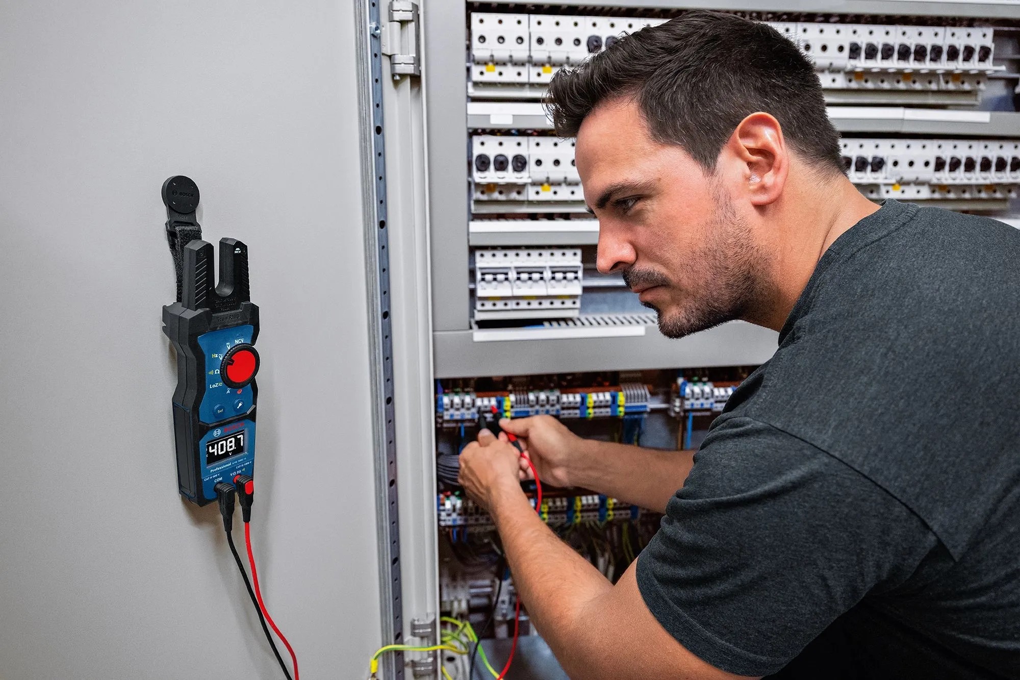 Vidlicový ampérmetr Bosch Professional GFM 1000-15 v provozu s elektrikářem u rozvaděče. Vidlicový ampérmetr Bosch Professional GFM 1000-15 v provozu s elektrikářem u rozvaděče.