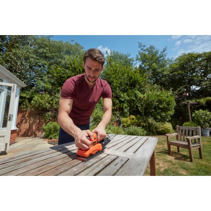 Muž brousí stůl s vibrační bruskou Black+Decker BEW220. Bruska v oranžové a černé barvě.