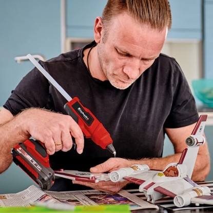 Muž používá akumulátorovou tavnou pistoli Einhell Power X-Change TE-CG 18 Li k modelování. Červená tavná pistole s akumulátorem.