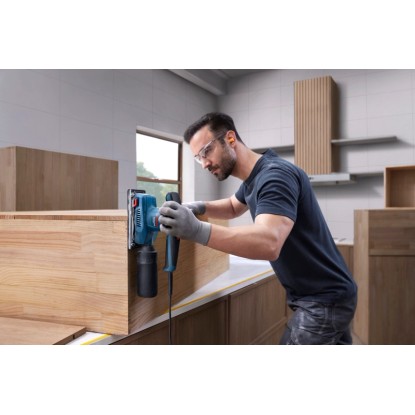 Muž brousí dřevo modrou vibrační bruskou Bosch Professional GSS 20-18 A v dílně.