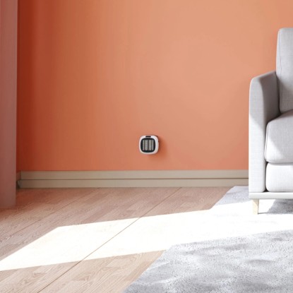 Kompaktní bílý zásuvkový ohřívač 700 W na barevné zdi v obývacím pokoji.