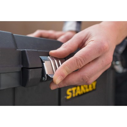 Detailní záběr: Ruka zavírá kovovou západku černé montážní bedny Stanley Essential Mobile (50 l).